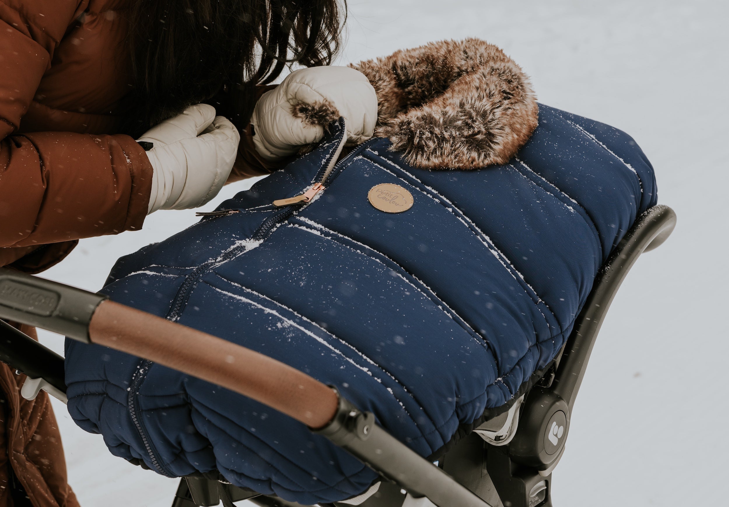 Mère qui se penche au-dessus de son bébé au chaud dans sa coquille recouvert de la housse d'hiver Petit Coulou lors d'une marche hivernale