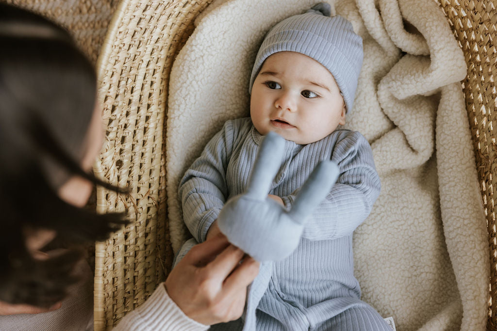 Mère qui veille sur son bébé nouveau-né couché dans son moïse vêtu de sa dormeuse et son bonnet bleu du coffret cadeau Petit Coulou