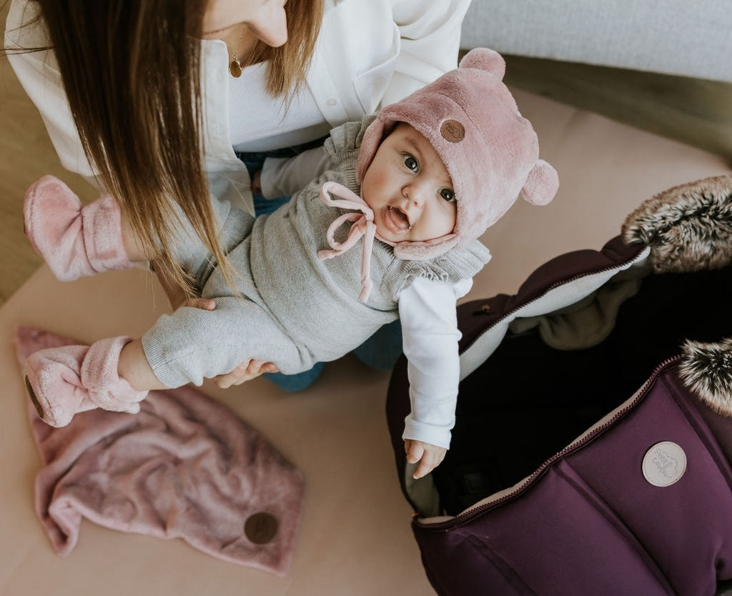 Maman avec bébé dans les bras qui porte les accessoires d'hiver pour nouveau-né Petit Coulou dans la couleur rose