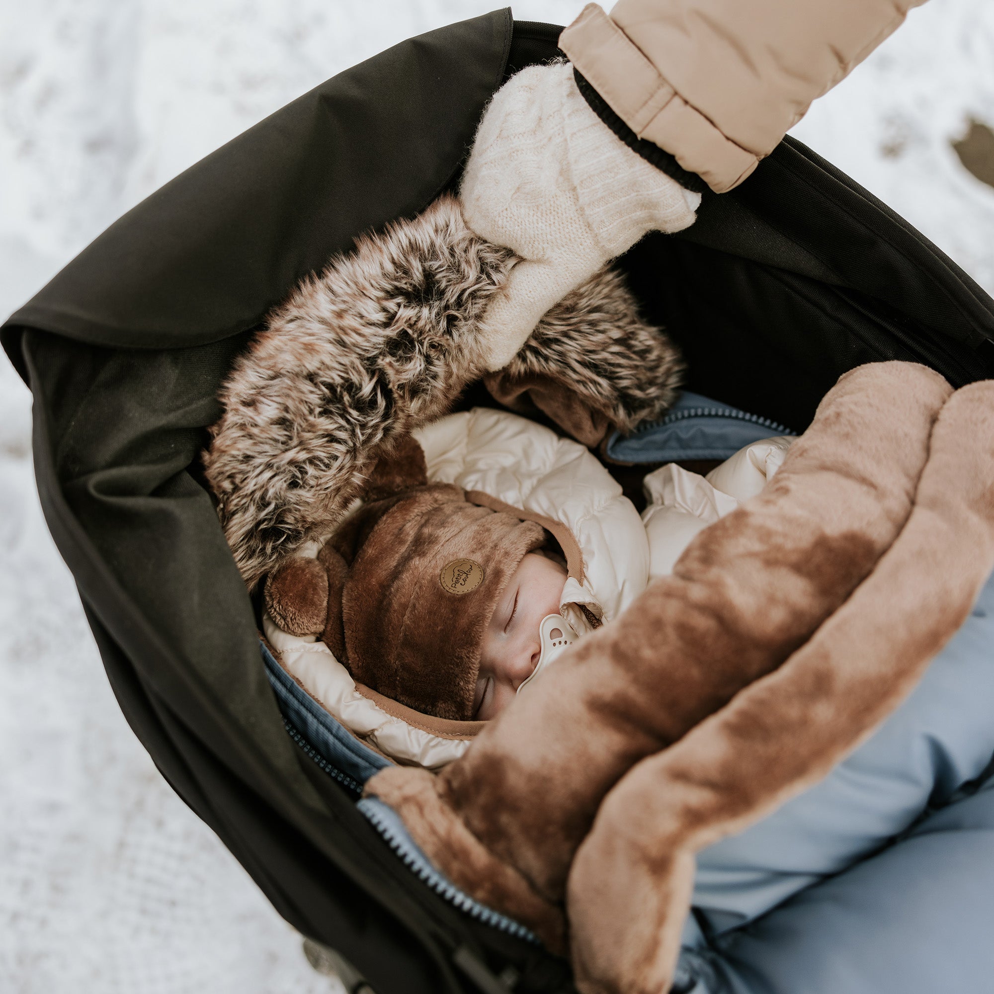 Vue d'un bébé dans un landau avec la housse chancelière cobalt et la tuque ourson couleur moka
