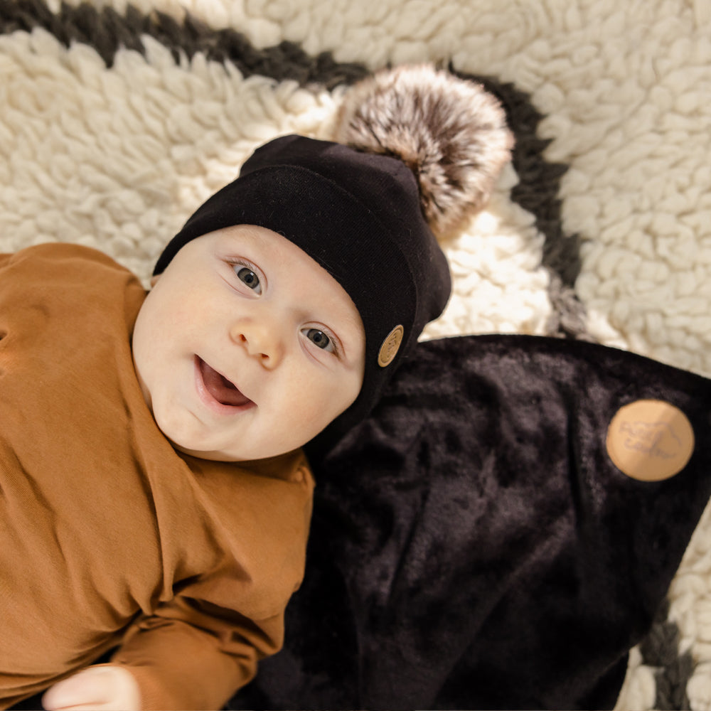 Baby with a black pompon beanie and a small blanket for baby car seat