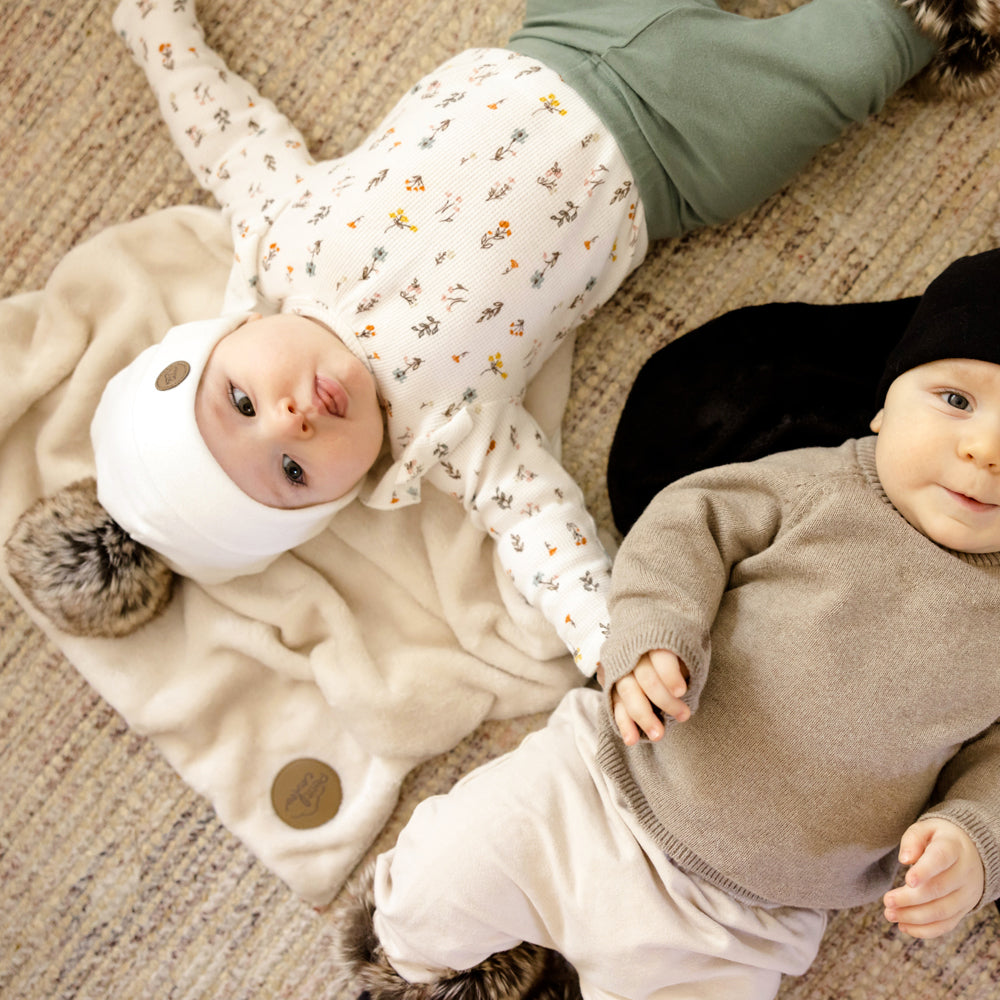 Enfant couchés sur le sol avec tuques pompon et doudou en fourrure synthétique crème et noire