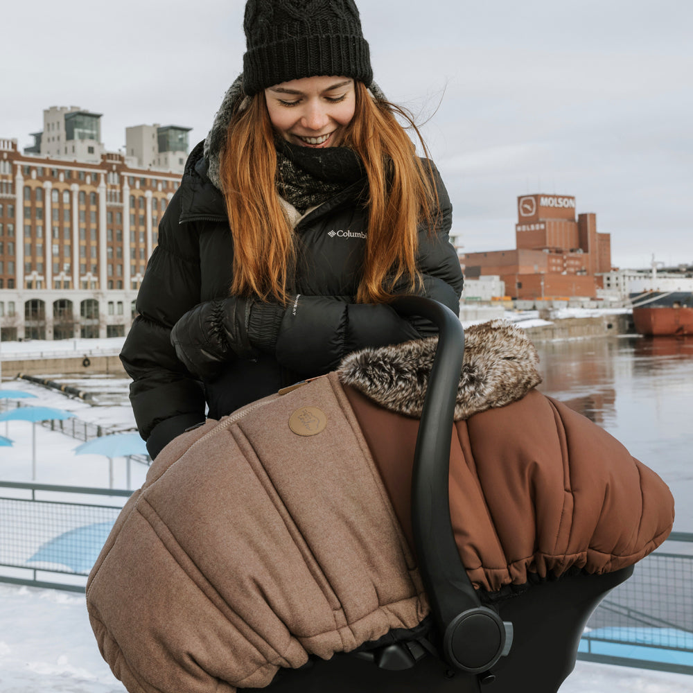 #color_choco-caramel#couleur_choco-caramel - Femme avec un manteau noire tenant une coquille avec une housse hiver brune pour banc d'auto de bébé