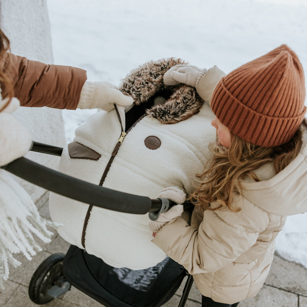Housse hiver Jasper sur coquille et poussette avec jeune fille qui tient le col en fourrure végane