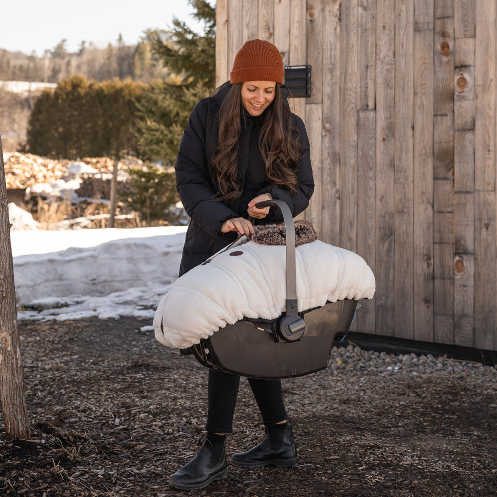 Maman avec tuque en tricot qui tient une coquille avec une housse en faux-mouton Jasper dans ses mains