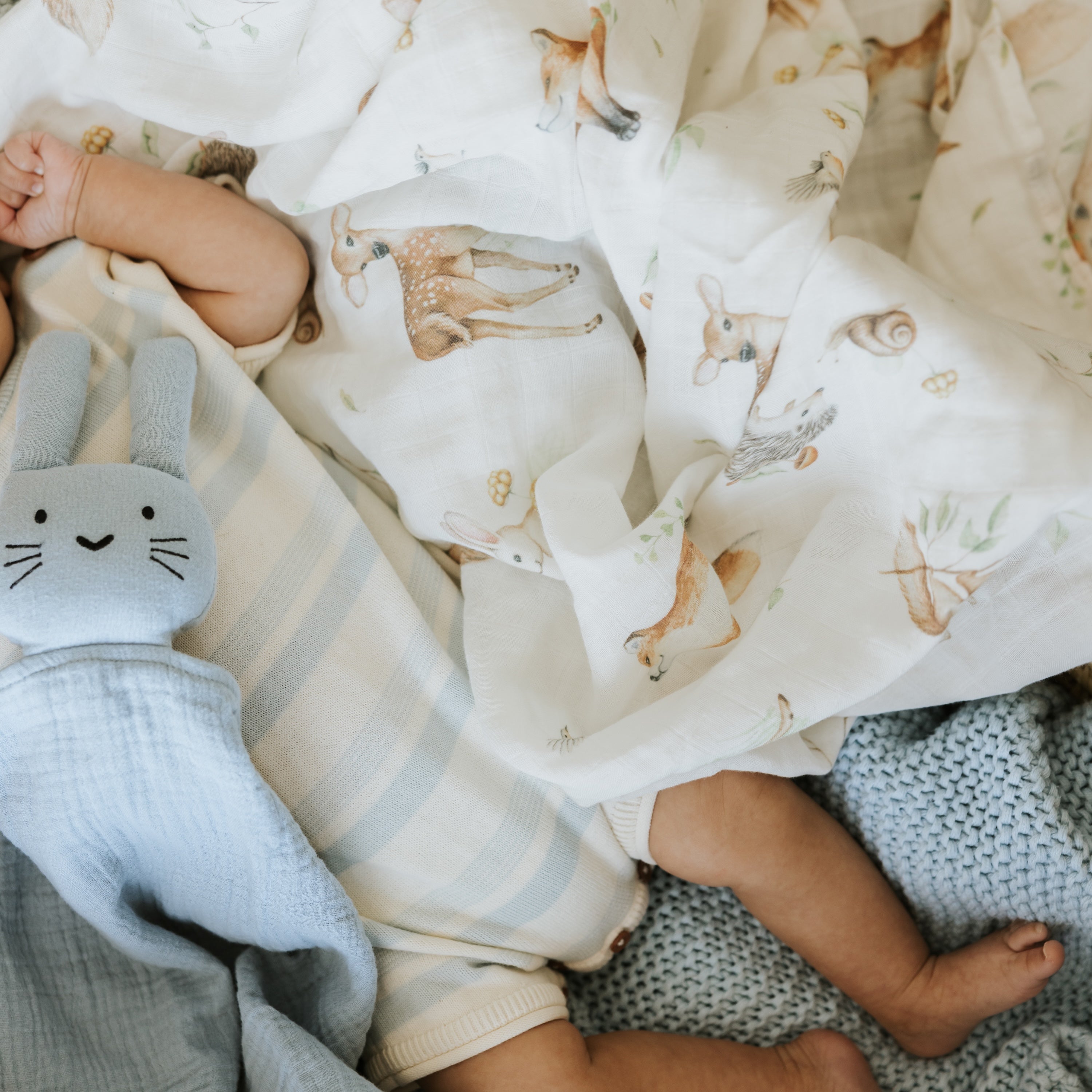 Bébé avec une peluche bleue et une couverture avec des motifs d'animaux de la forêt