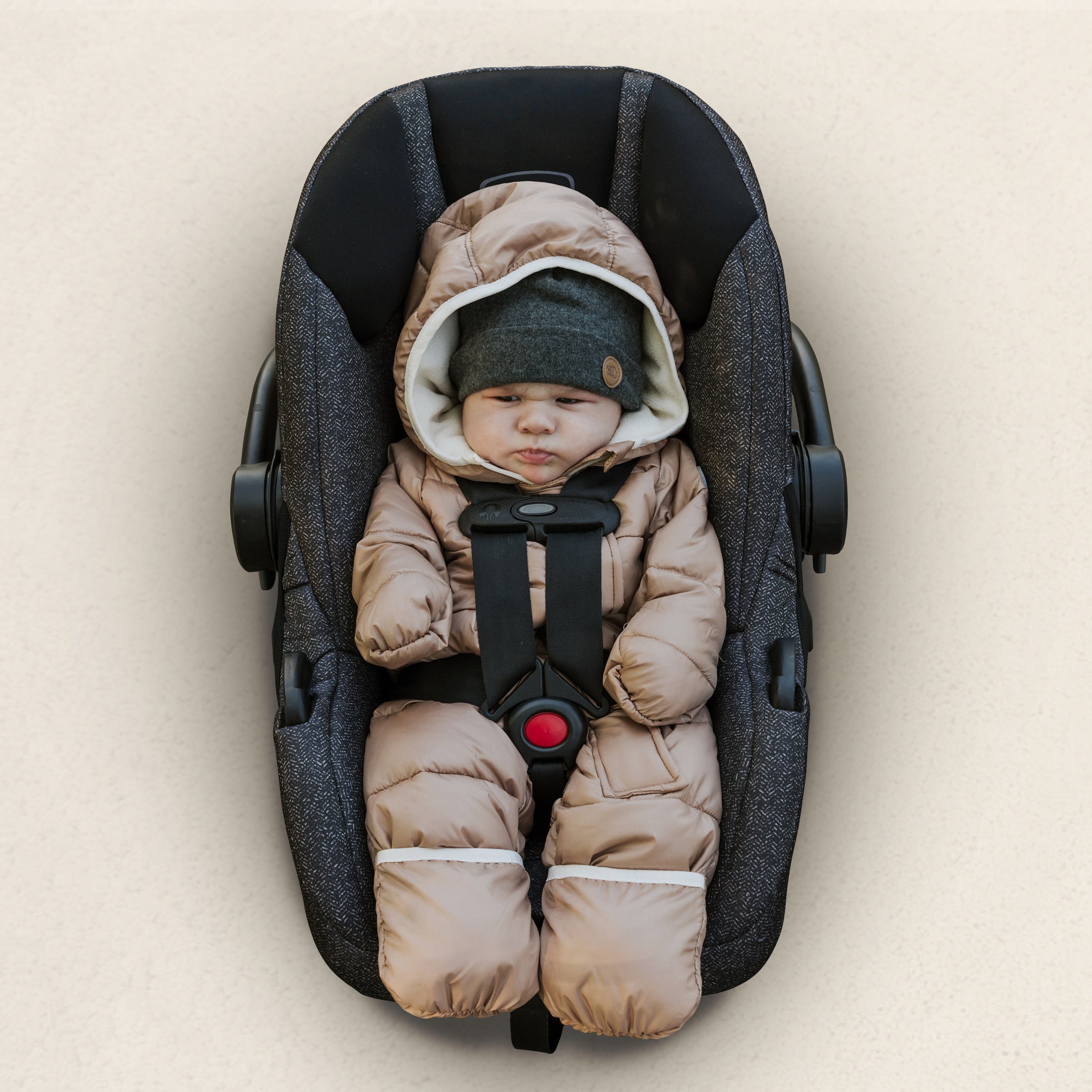 Angry baby in his car seat with a bulky snowsuit and a pompom beanie