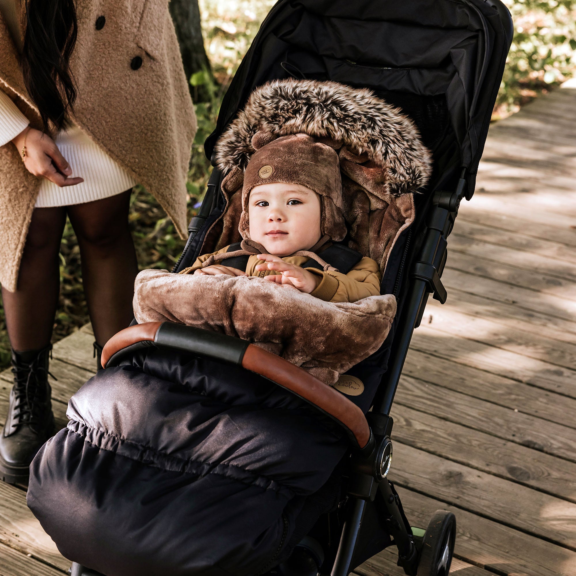 Jeune enfant avec tuque ourson en minky brune dans la housse Chancelière noire pour poussette Petit Coulou