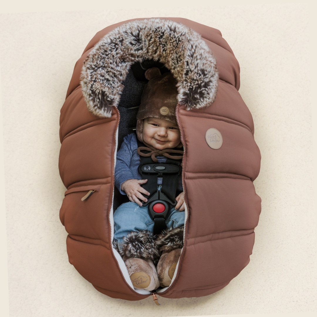 Happy baby in his car seat with a Petit Coulou winter cover, a teddy bear hat and booties