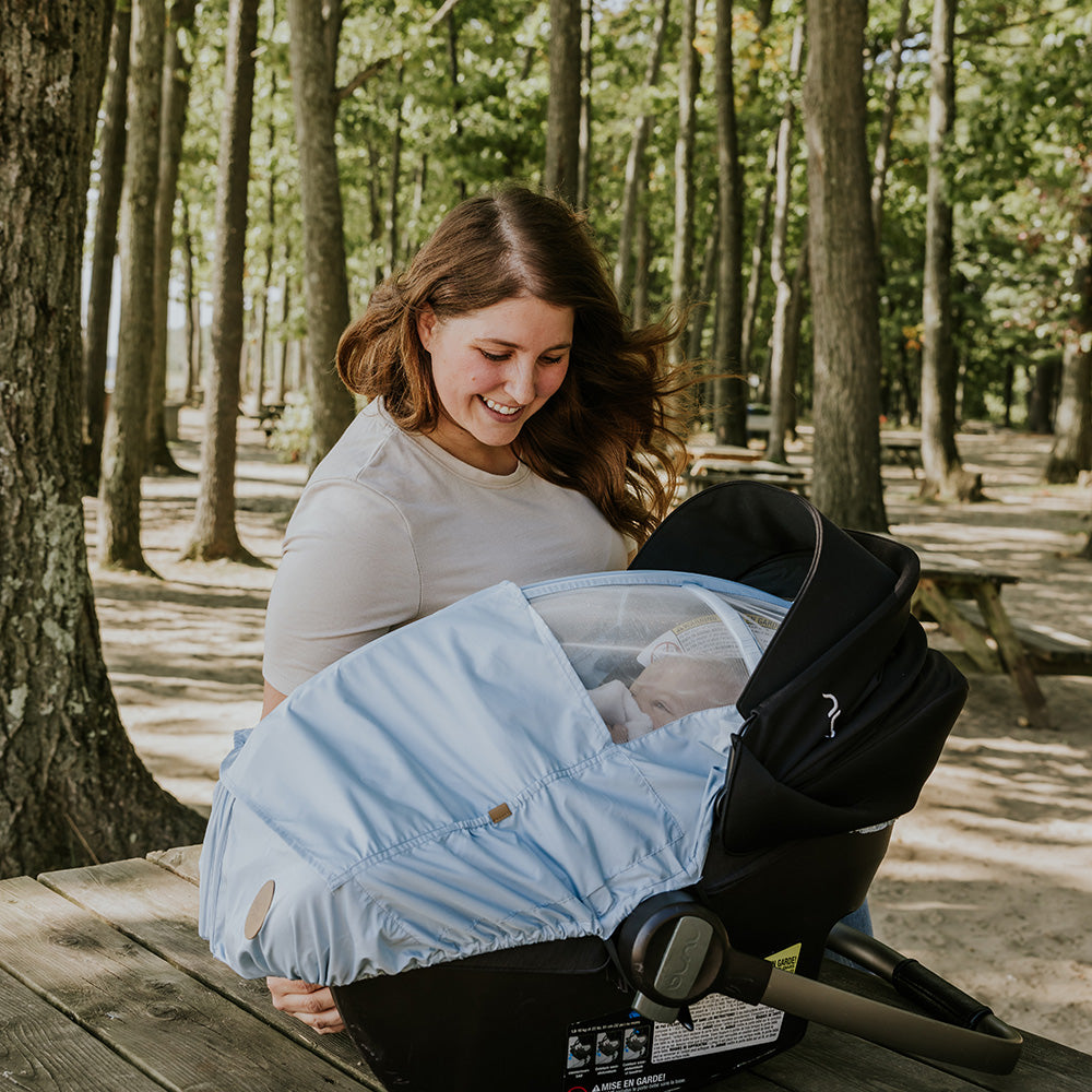 Maman qui veille sur son bébé assis confortablement dans sa coquille recouvert d'une housse d'été Petit Coulou bleu poudre