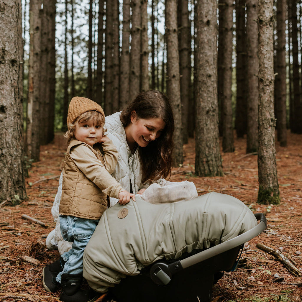 Maman et petit frère dans une forêt qui veille fièrement sur bébé couché dans sa coquille recouvert d'une housse légère lichen Petit Coulou