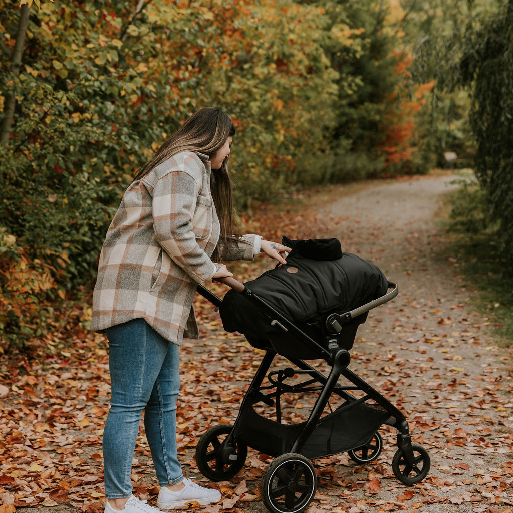 Maman qui veille sur son bébé couché dans sa coquille recouvert d'une housse légère noire Petit Coulou lors d'une marche automnale