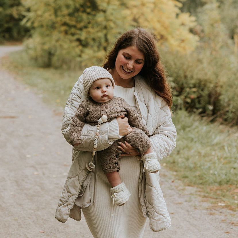 Maman qui tient son bébé dans ses bras lors d'une marche automnale portant sa tuque en tricot beige Petit Coulou
