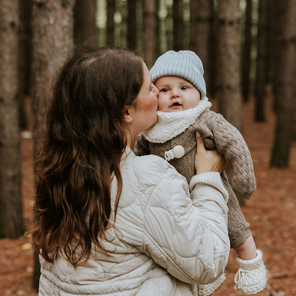 Mère qui donne un bisou sur la joue de son bébé qui porte une tuque en tricot bleue Petit Coulou