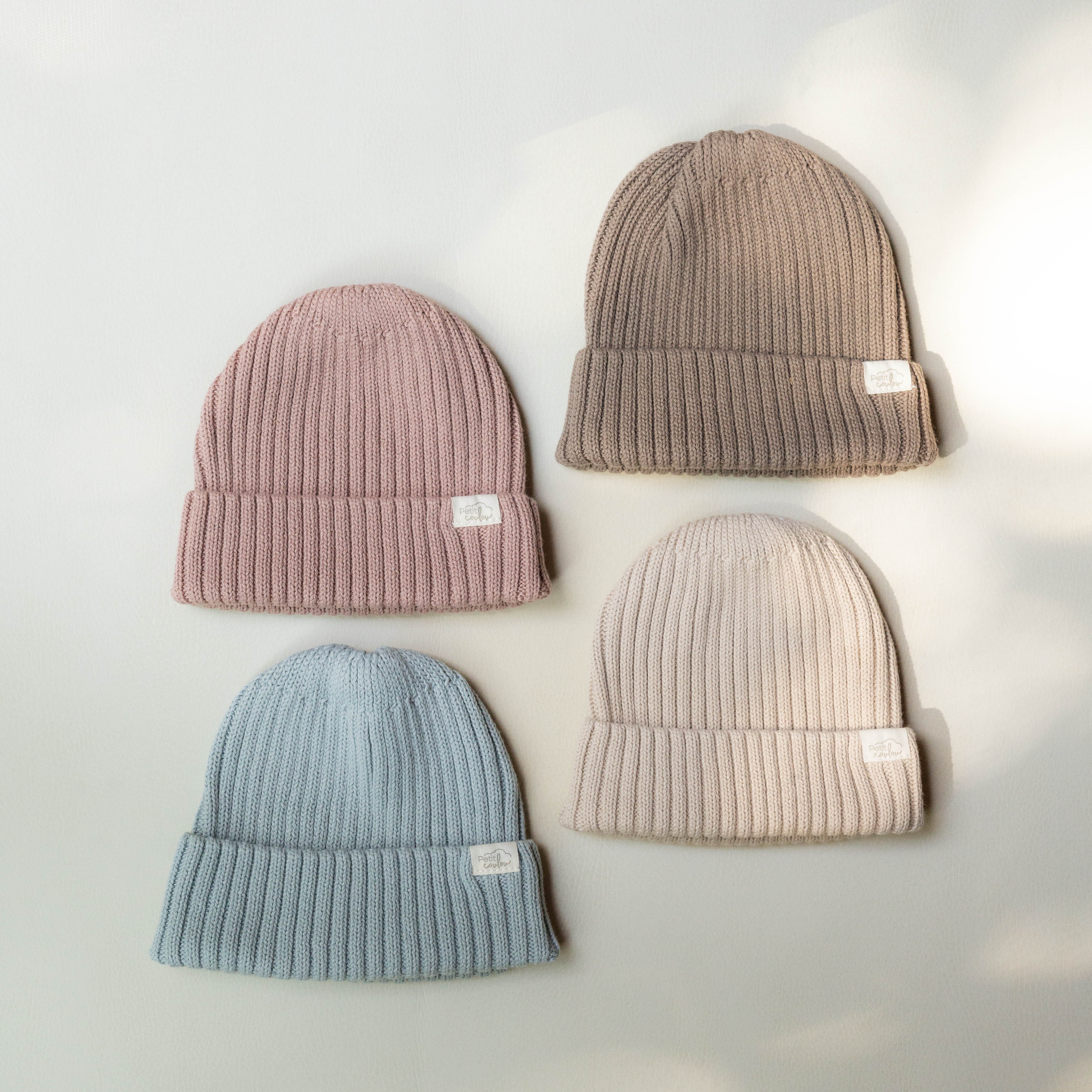 Les 4 couleurs des tuques en tricot Petit Coulou pour bébé présenté à plat