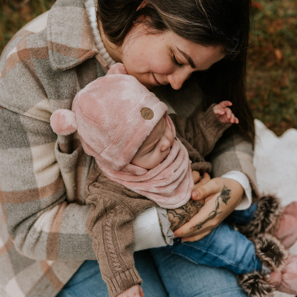 Mère qui tien son bébé dans ses bras portant une tuque ourson, un cache-cou et des bottines douces en minky rose de Petit Coulou