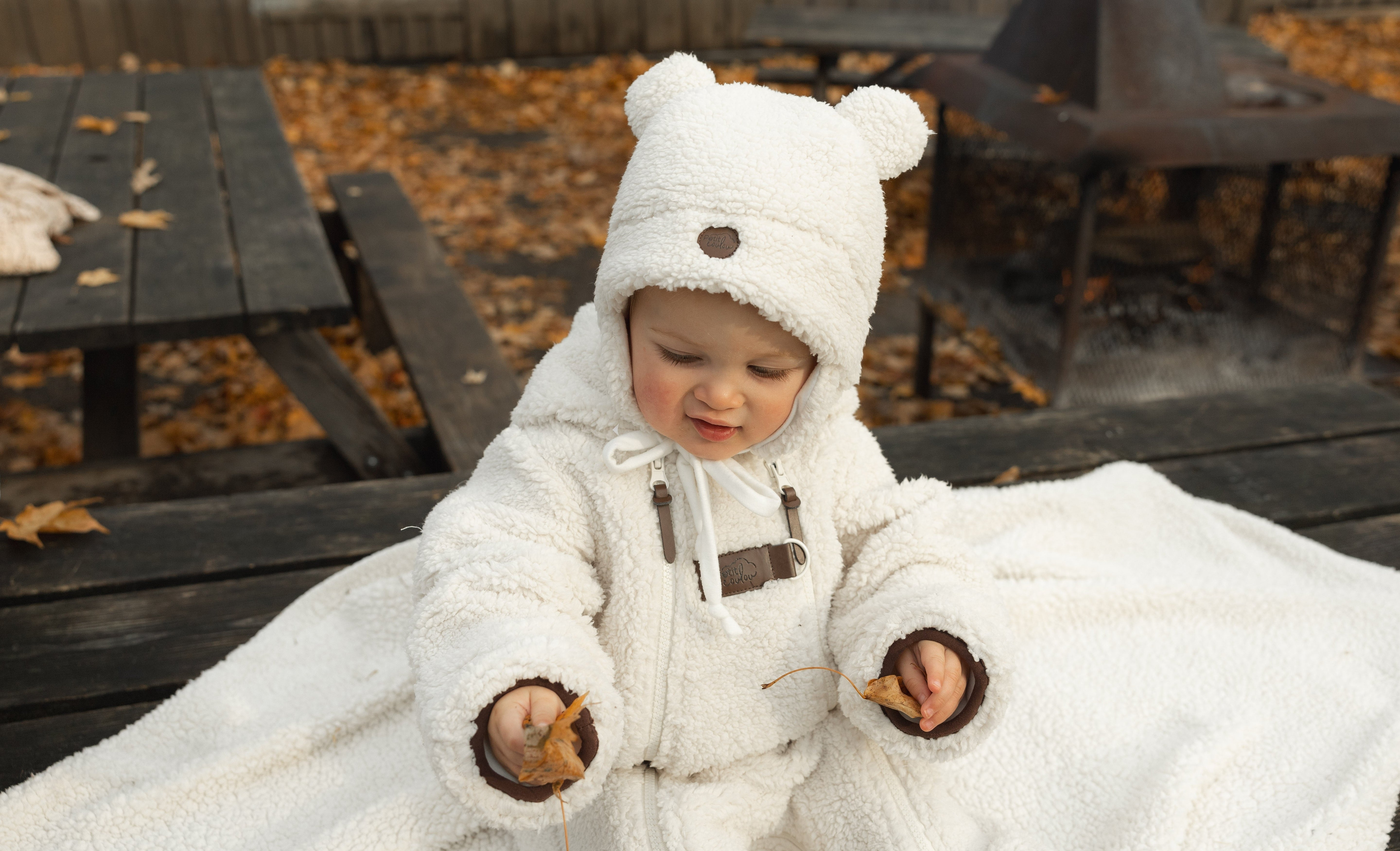 Bébé assis sur une table picnic extérieure en automne portant une combinaison chaude et une tuque en sherpa ourson