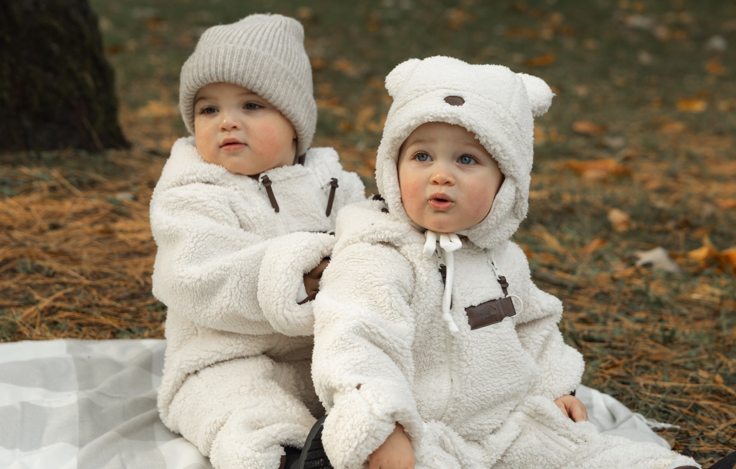 Deux bébé assis ensemble sur une couverture dans les feuilles d'automne vêtus de la combinaison onesie en sherpa Petit Coulou