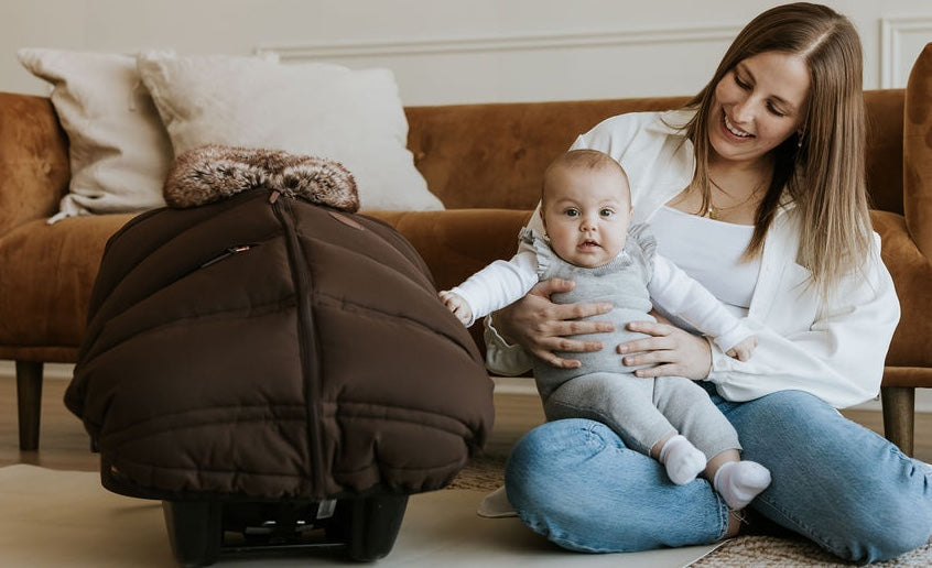 Bébé et maman assis ensemble dans le salon près de sa coquille recouvert d'une housse d'hiver Petit Coulou dans la couleur café