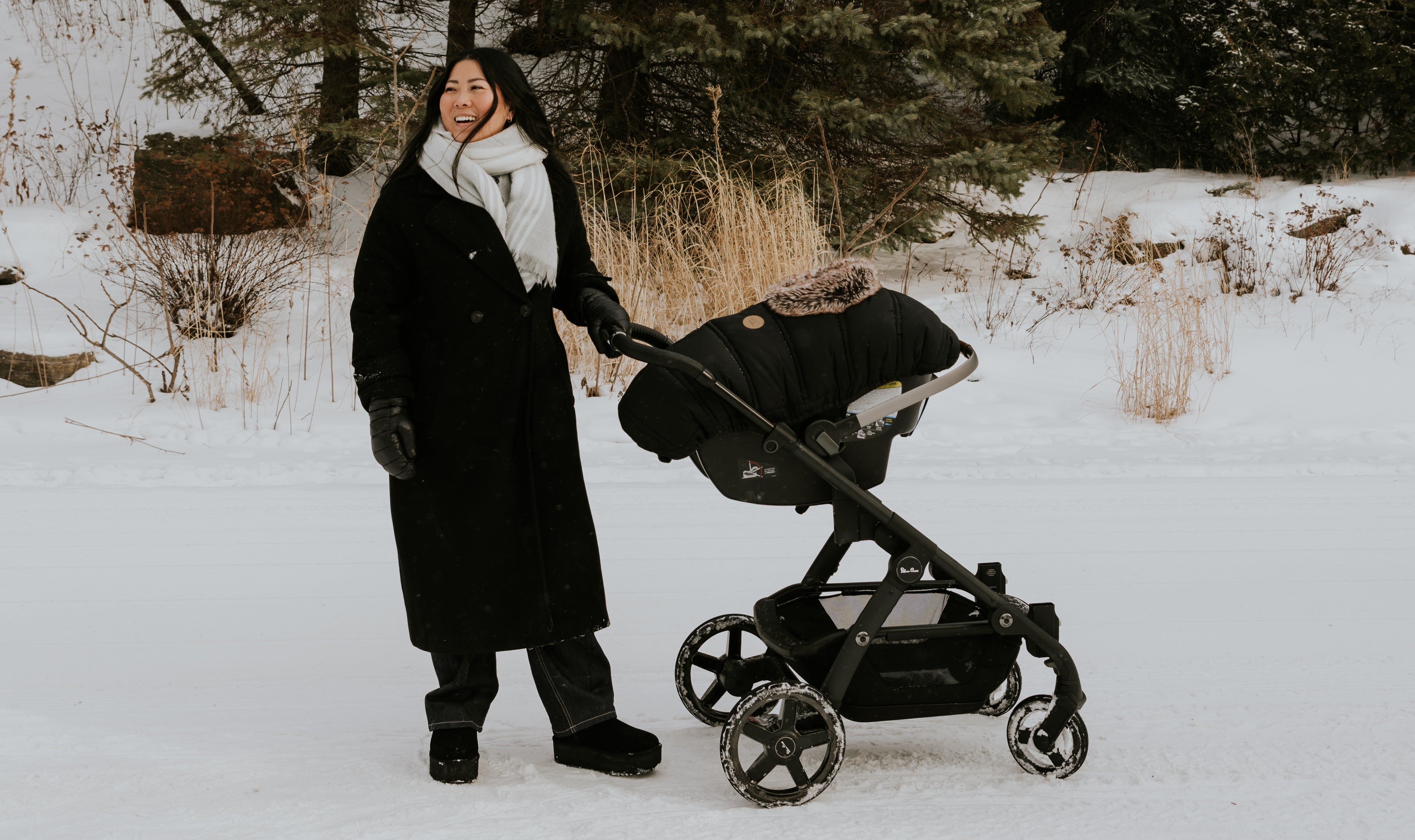 Mère qui pousse la poussette de son bébé lors d'une marche hivernale et profite du beau temps grâce à la housse d'hiver pour coquille Petit Coulou