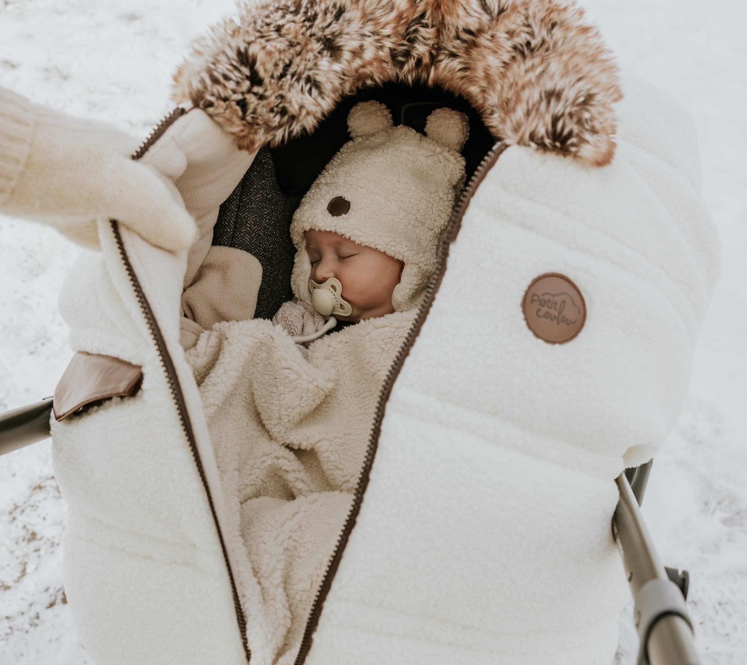 Bébé qui dort au chaud dans sa coquille et sa housse d'hiver Petit Coulou en sherpa lors d'une marche hivernale
